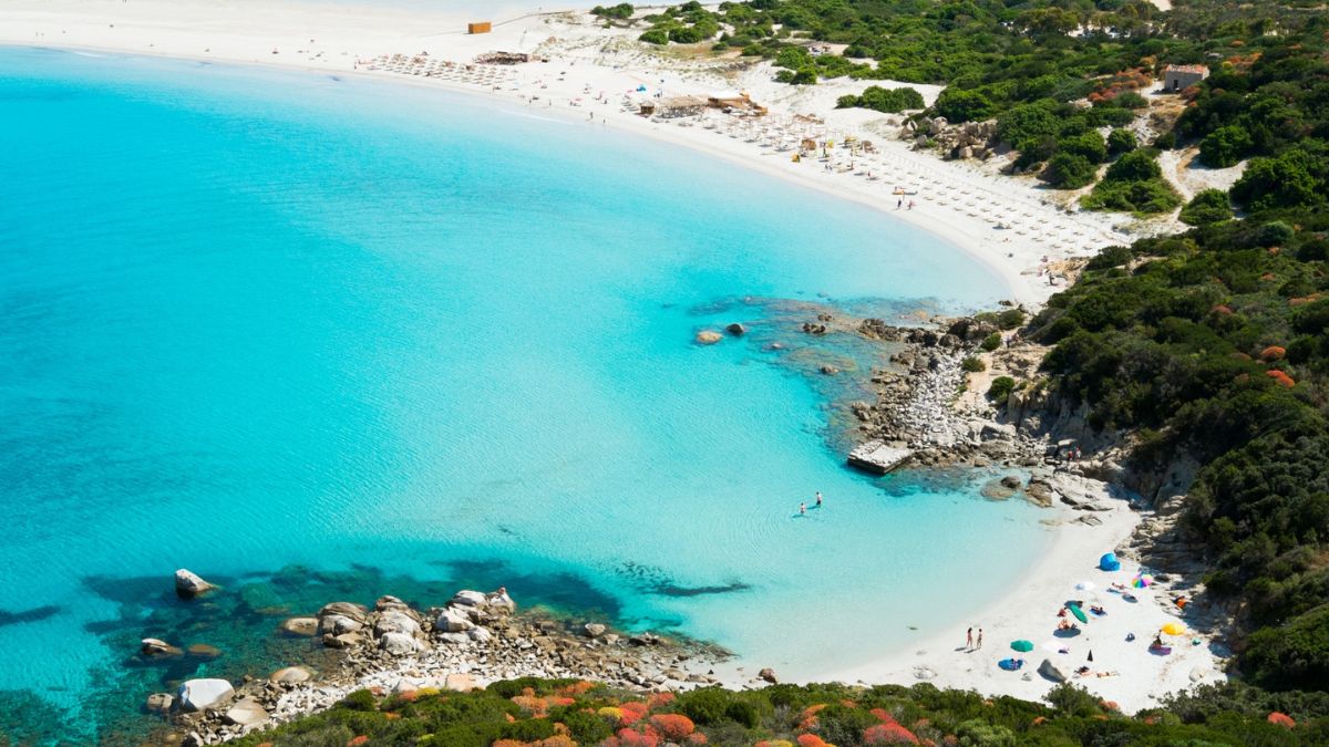 Spiaggia tranquilla in Sardegna, con acqua cristallina e sabbia bianca, lontana dal turismo di massa.