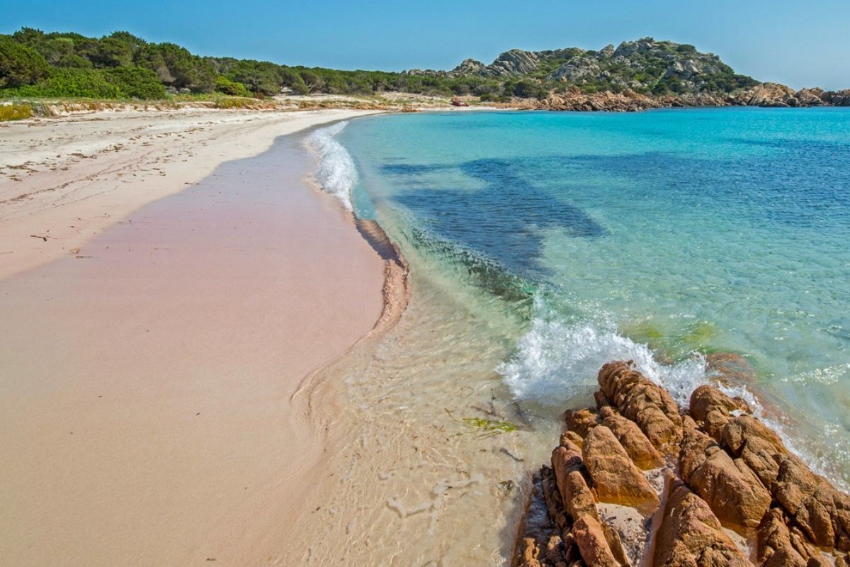 Spiaggia rosa in Sardegna con sabbia corallina e mare cristallino, incantevole panorama naturale.